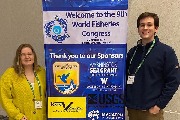 Kylee Wilson and Andrew Foley on either side of a sign for the World Fisheries Congress