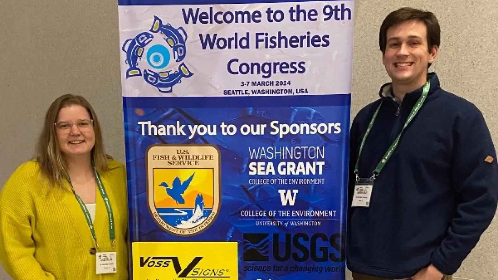 Kylee Wilson and Andrew Foley on either side of a sign for the World Fisheries Congress