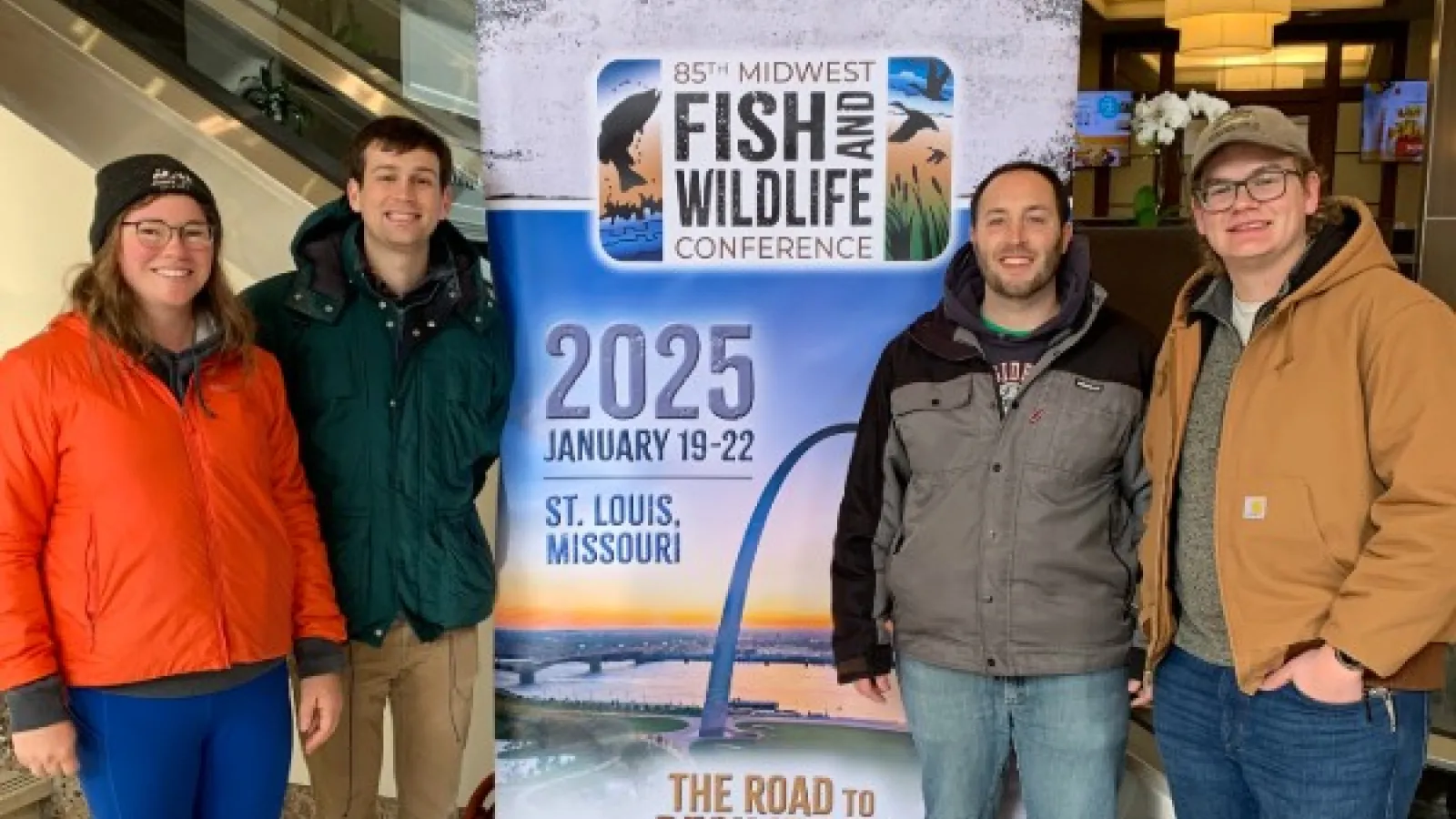 Shaley Valentine, Andrew Foley, Steven Gratz, and Jacob Bentley in front of a sign for the Midwest Conference