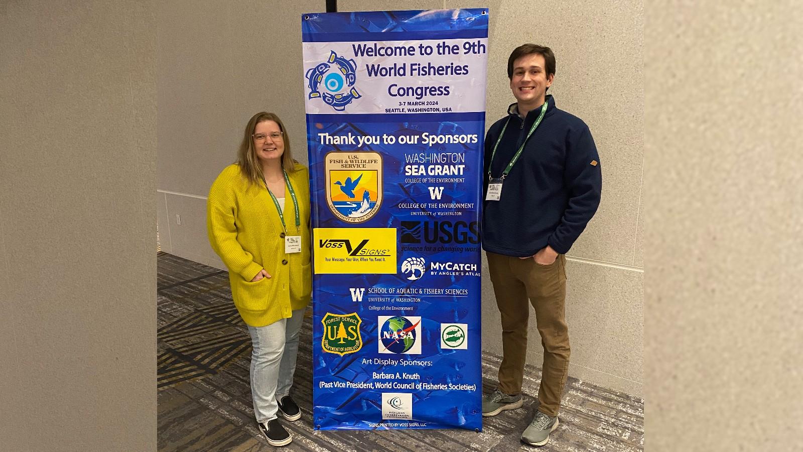 Kylee Wilson and Andrew Foley on either side of a sign for the World Fisheries Congress