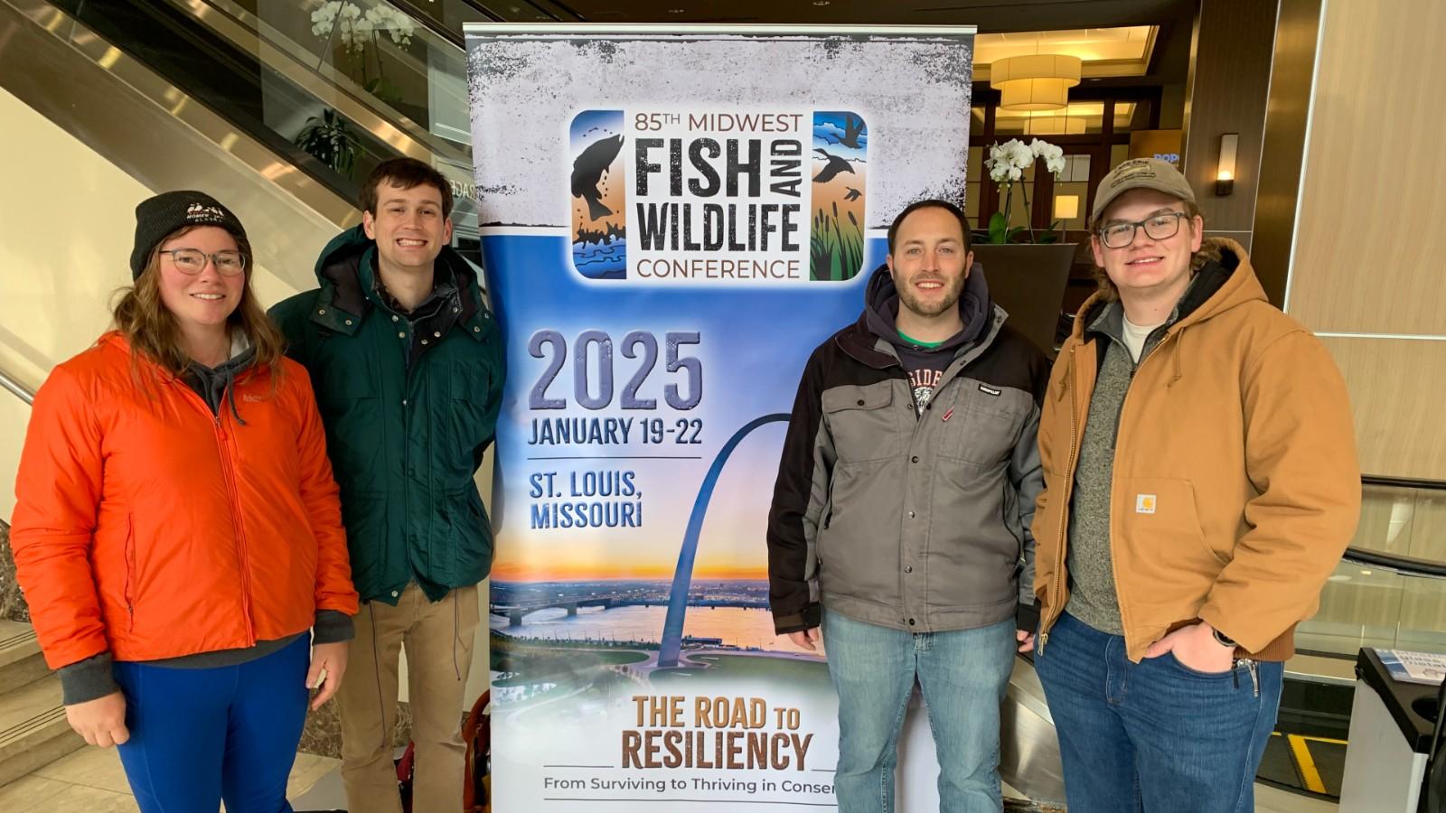 Shaley Valentine, Andrew Foley, Steven Gratz and Jacob Bentley in front of the Midwest conference banner