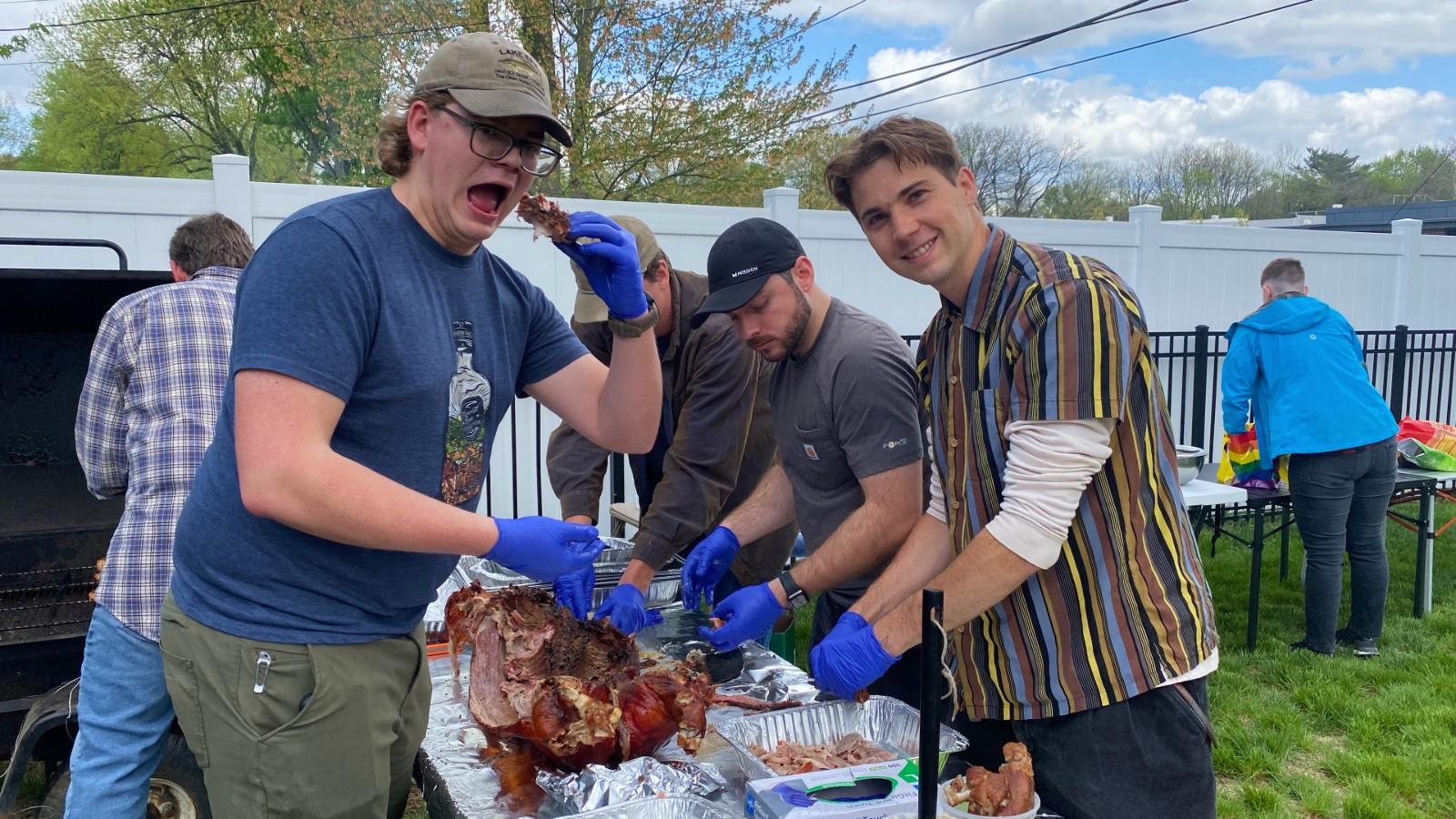 Jacob taking a bit while he, Sawyer, Matt, and Neil process the cooked pig