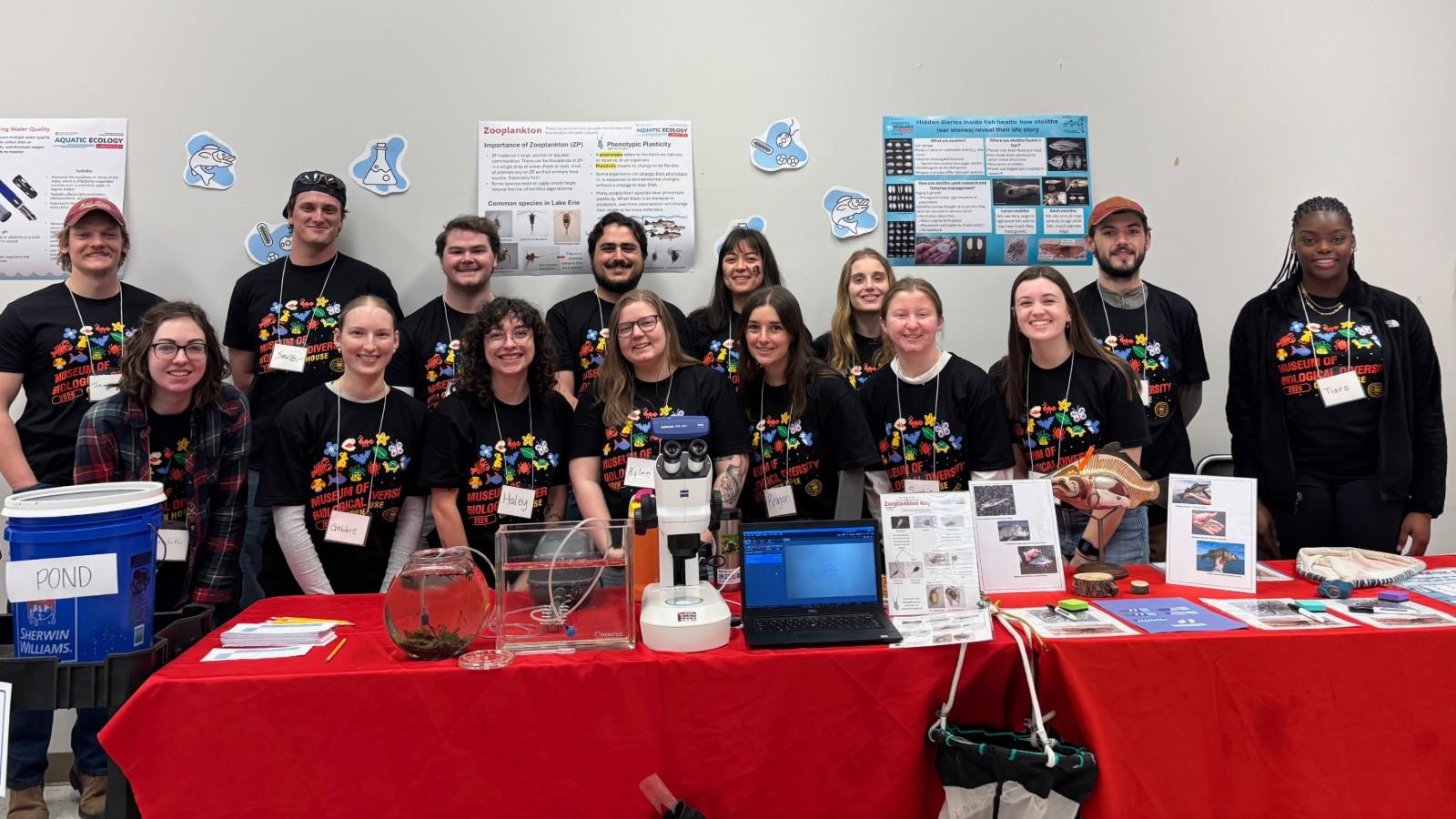 Posed group of AELers behind display tables at the start of open house